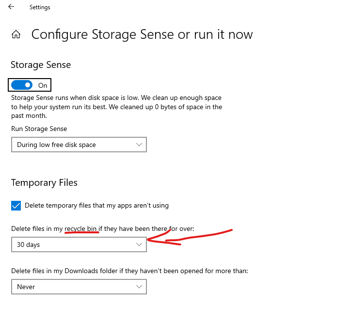 Windows 10 Configure Storage Sense or run it now screen. Storage sense is on, and the "Delete temporary files that my apps aren't using" is selected. "Delete files in my recycle bin if they have been there for over: has the words "recycle bin" underlined, and then an arrow points at the selection box where 30 days is selected.