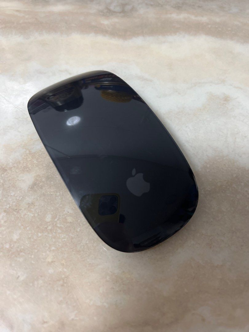Top view of black apple magic mouse on a tan countertop.