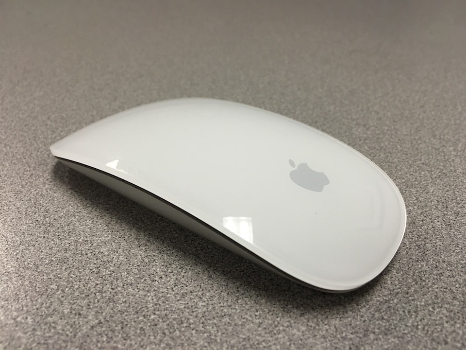 Top view of a white apple magic mouse on a grey surface. 
